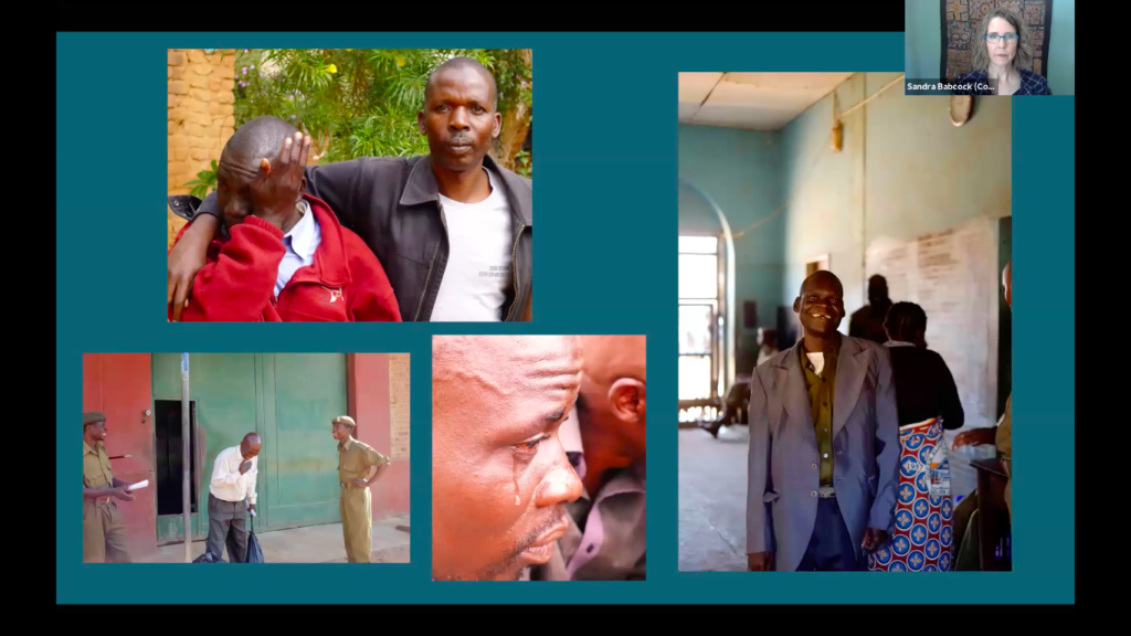 A woman in a video conference, pictured in a small rectangle in the upper righthand corner, looks serious. The rest of the screen shows four photographs. In one photo, a man puts his shoulders around another man, who is wiping his eyes. In another photo, a man holds a hand to his heart as he stand in front of a building between two men dressed in all green. In another photo, a tear falls down a man's cheek. In the final photo, a man wearing a dress shirt smiles at the camera.
