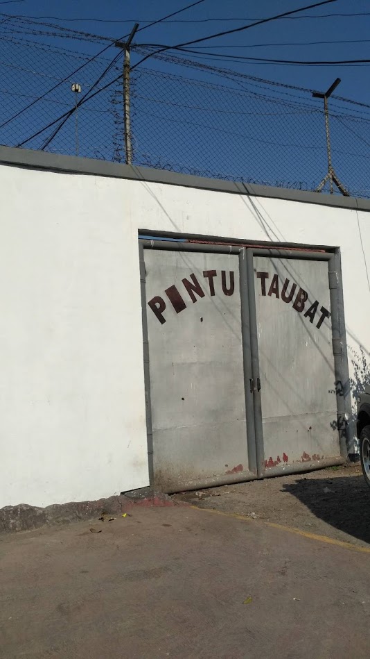 A white wall with a gray door on it. The gray door has the words "Pintu Taubat" written on it.