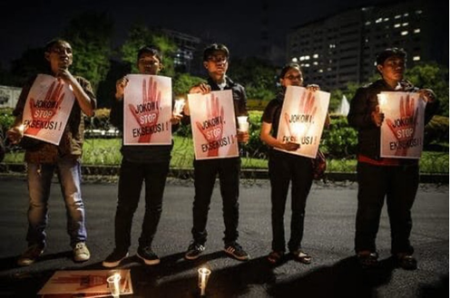 Five people stand in a row on a street at night. They are holding signs that demand an end to executions, and holding candles.